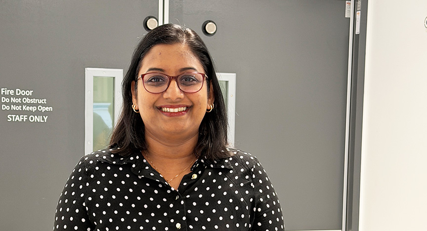 A woman in red glasses and a black shirt with white spots stands in front of the entrance to the Department of Cardiology