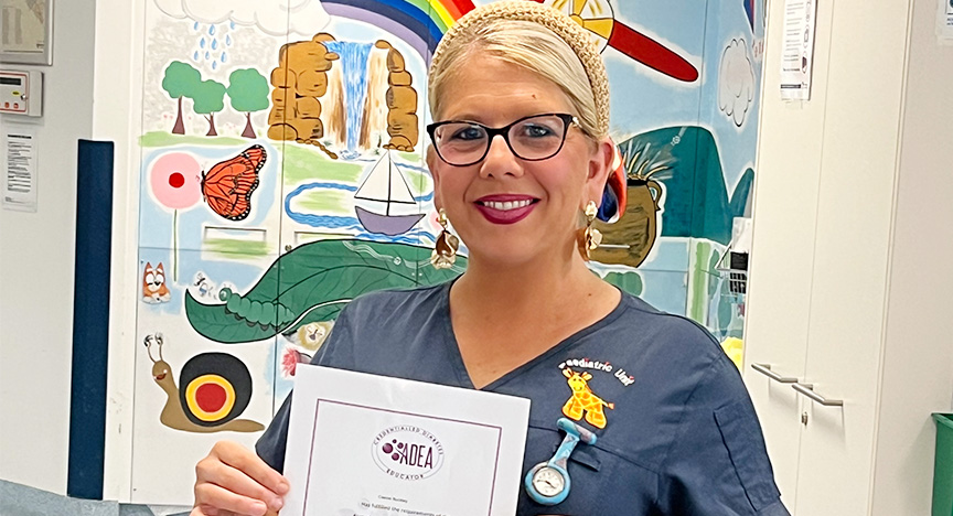 Newly credentialled diabetes educator Cassie wears a navy scrub top and holds a certificate,