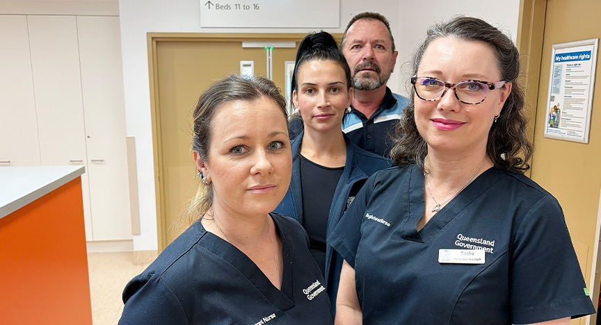 Hospital staff wearing navy uniforms stand together in a hospital ward.