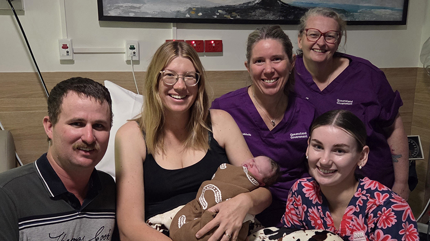 Mum with baby in hospital bed, with dad beside her and three midwives standing next to the bed, all smiling at camera.