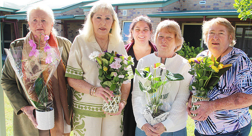 Four retiring staff stand in a line in the aged-care home's garden, holding flowers, with the director of nursing standing in the centre behind.