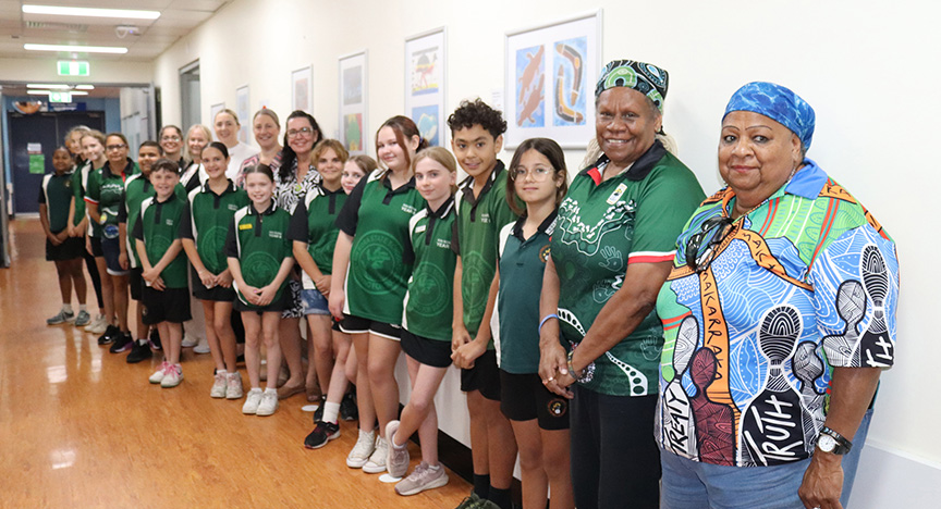 School students, staff, and hospital staff standing in smiling in front of a range of artworks on the wall.