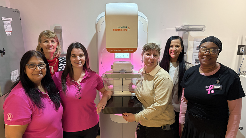 BreastScreen staff smiling at camera standing next to mammogram machine