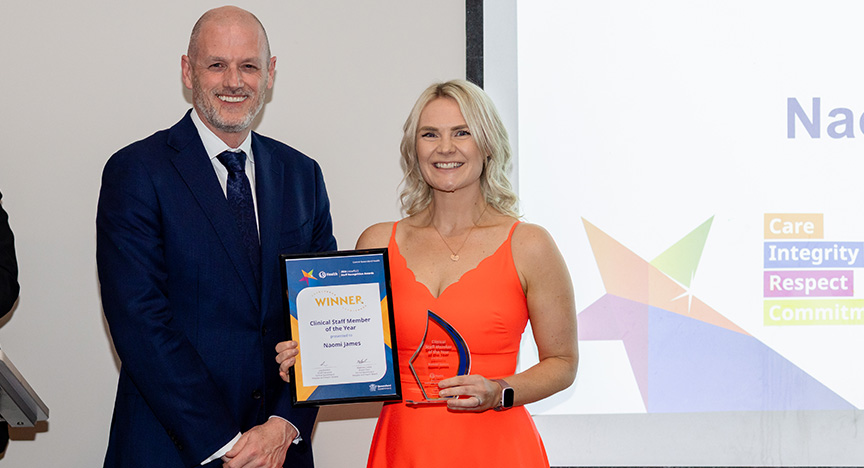 A man in a black suit presenting an award to a lady in an orange dress.
