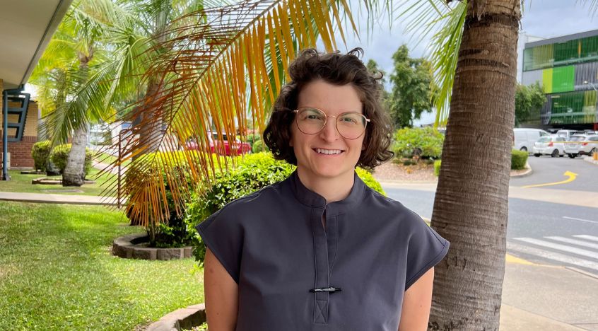 Female doctor wearing navy scrubs stands in garden for photo