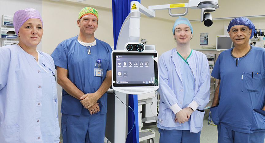 Gladstone Hospital perioperative staff members are excited to be utilising the state-of-the-art Teladoc system. Pictured from left Clinical Nurse Julie Gorse, Director of Surgery and Senior Staff Specialist Dr Darren Lituri, PHO Anaesthesia Dr Alexander Kelly and Staff Specialist General Surgery Dr Faris Alaswad. Nurse wearing sky blue scrubs and a purple scrub hat, surgeon wearing navy scrubs and a green scrub hat, trainee surgeon wears sky blue scrubs and scrub hat, and a surgeon wears navy scrubs and scrub hat. All standing near telehealth equipment in an operating theatre.