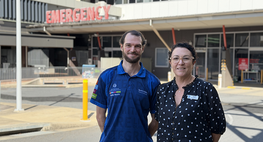 A doctor and nurse standing in front of Rockhampton Hospital's Emergency Department entrance, smiling at camera.